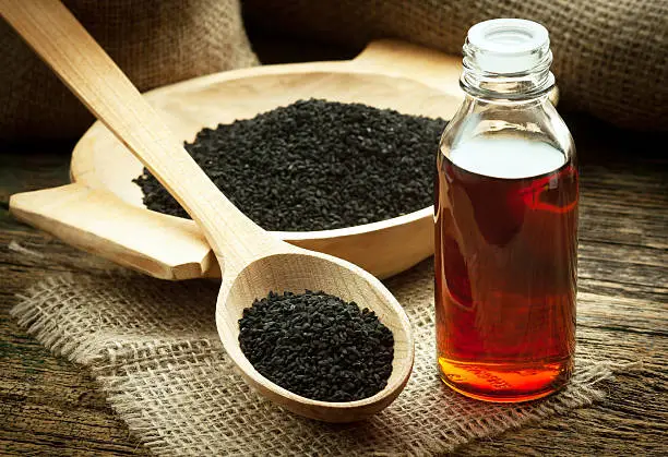 Nigella sativa (Black cumin) on wooden spoon and essential oil. Real oil from nigella looks like dark honey