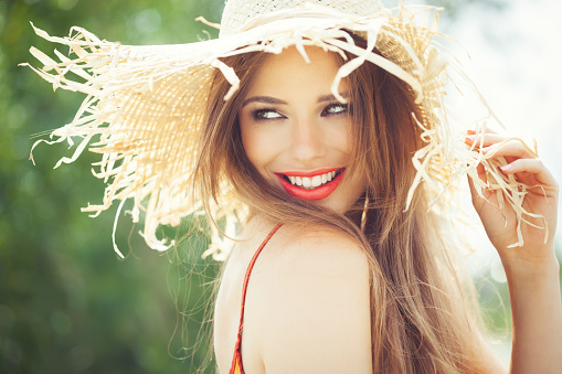 Young woman in straw hat smiling in summer outdoors.
