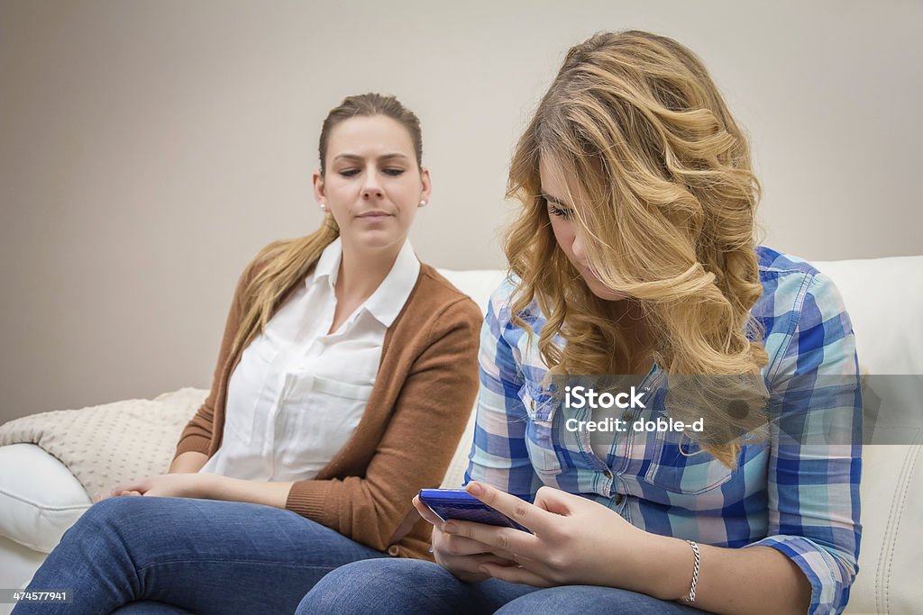 Suspicious mother spying a daughter looking phone Suspicious mother spying her teenage daughter while looking messages in a smartphone. Bad family communication concept by new technologies Mother Stock Photo