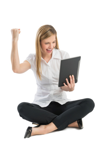Full length of cheerful young businesswoman with digital tablet celebrating success while sitting on floor against white background
