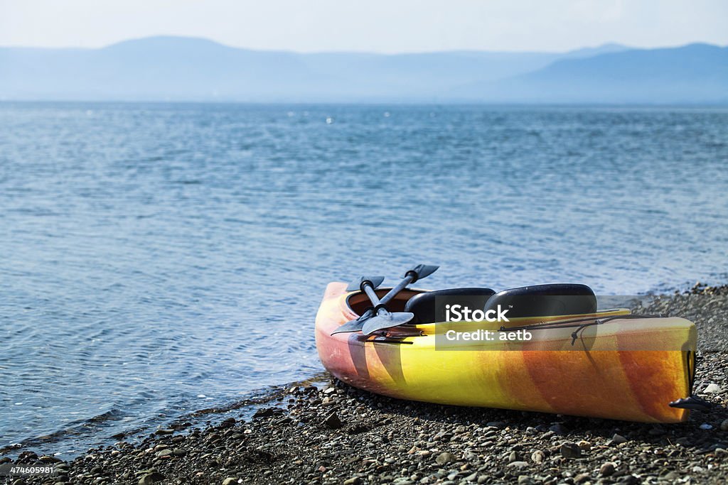 Orange and Yellow Kayak With Oars on the Sea Shore Orange and Yellow Kayak With Oars on the Sea Shore During a beautiful Day of Summer Activity Stock Photo