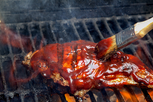 Chicken breast on an old fashioned charcoal grill with leaping flames.  Meat is being basted with barbecue sauce with a brush.