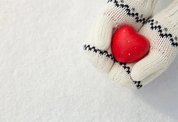 Close up of little girl's hands holding red rubber heart on the snow with copy space