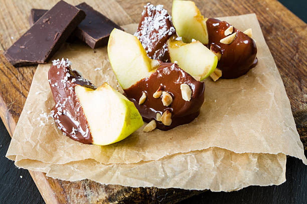 A row of green chocolate coated apples on sticks displayed at a christmas market sweets stall, with colorful treats visible in the background.