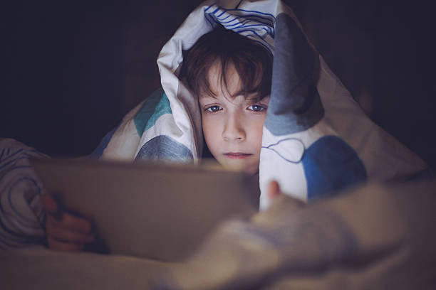 istock Boy lying in bed and playing at a digital tablet 474626476