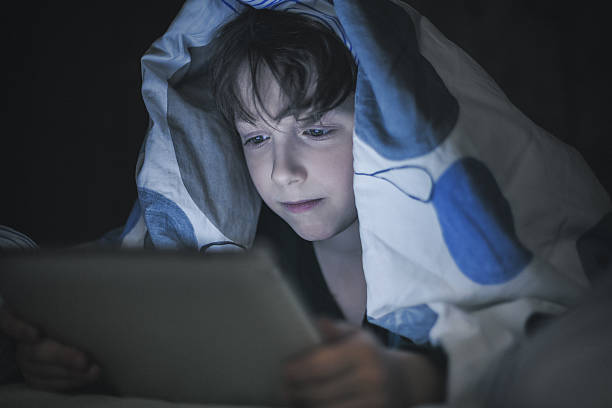 istock Boy lying in bed and playing at a digital tablet 474626478