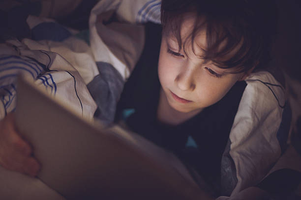 istock Boy lying in bed and playing at a digital tablet 474626482
