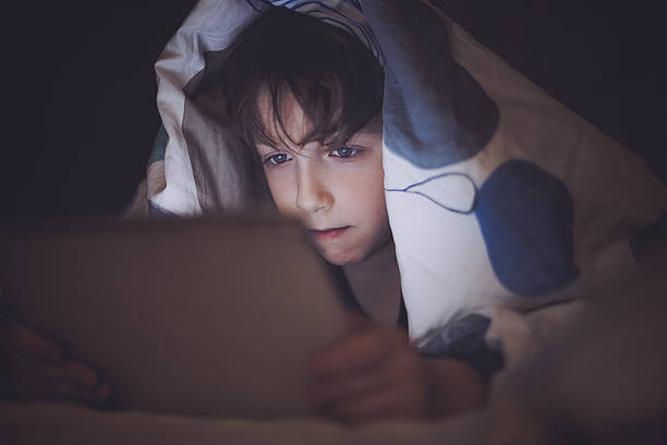 istock Boy lying in bed and playing at a digital tablet 474631474
