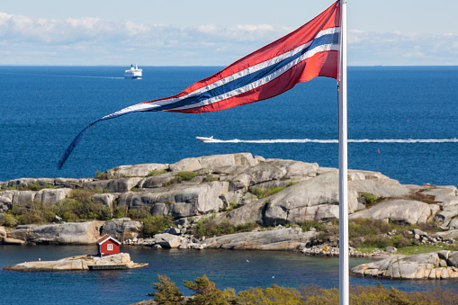 Norwegian flag with a pretty cabin on an island with a speed boat and ferry in the background