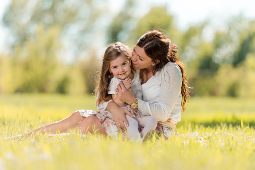 Happy mother kissing her little girl and enjoying with her in the park.