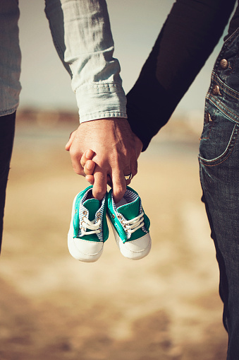 Future parents holding hands and a pair of little shoes