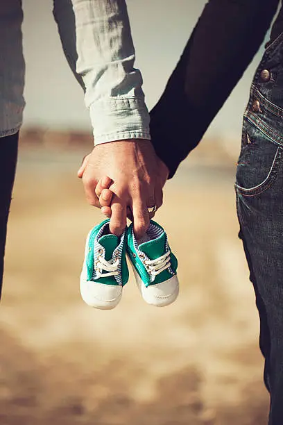 Photo of Future parents holding hands and a pair of little shoes