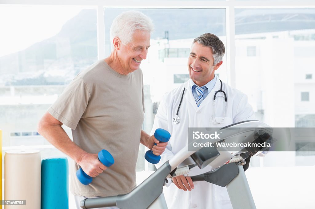 Senior man on treadmill with therapist  Senior man on treadmill with therapist in fitness studio  Doctor Stock Photo