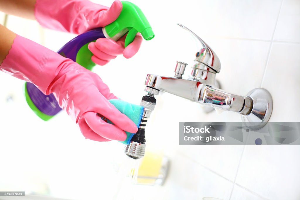 Cleaning bathroom faucet. Closeup of unrecognizable person's hand in a pink glove cleaning bathroom faucet with blue cloth and detergent in plastic bottle.and This is regular procedure in domestic bathroom. 2015 Stock Photo