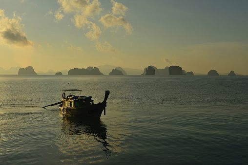 A long boat approaching the Thakhao pier with the Pakoh limestone islands in the distance part of the Phang Nga National park at sunrise.