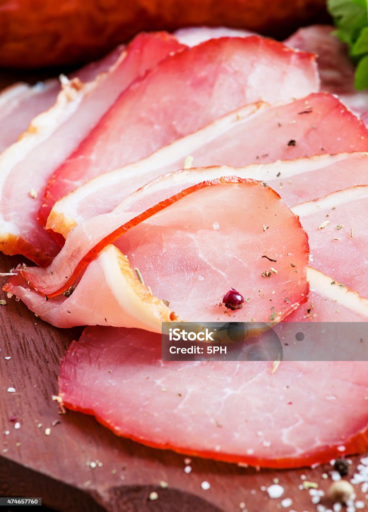 Slices of smoked ham and sausages on a cutting board Slices of smoked ham and sausages on a cutting board in a rustic style, selective focusSlices of smoked ham and sausages on a cutting board in a rustic style, selective focus 2015 Stock Photo