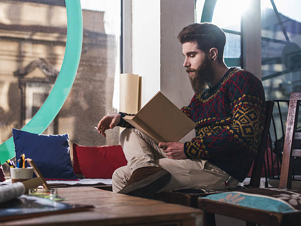 istock Young hipster reading a book and holding a cigarette. 474671104