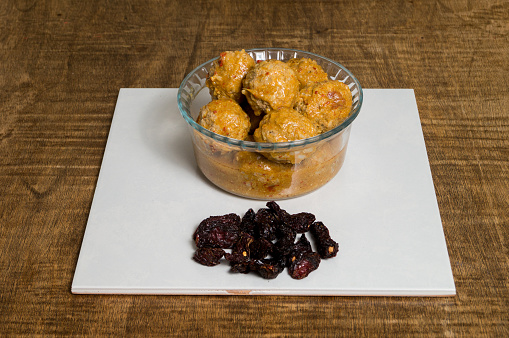 A crystal bowl of Mexican Meat Balls (albóndigas in Spanish). Cooked with chipotle chili. Dry chipotle chili stack. Served over a wooden table.  The dish is called in México Albondigas al chiplote.