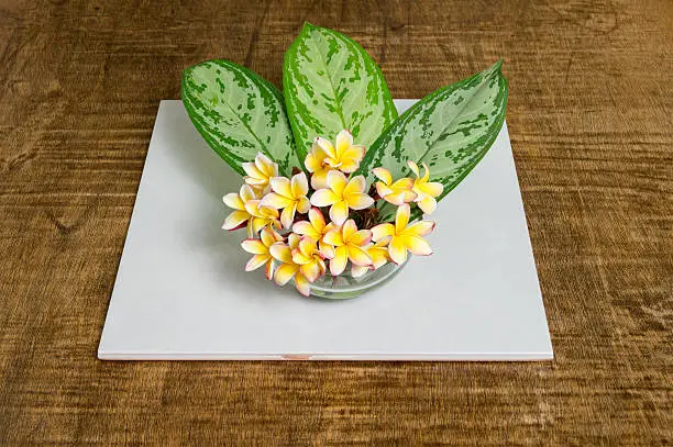 A bouquet of may flowers with green leaves in a crystal plant pot over a dark wooden table.
