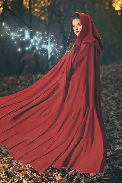 Beautiful woman with red flying cloak posing in the woods
