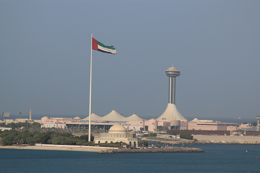 View of modern buildings in Abu Dhabi, in the United Arab Emirates, symbolized by Arabian tent structures with the flag of the United Arab Emirates blowing in the breeze