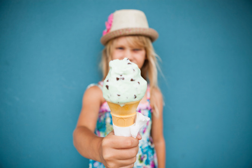 Closeup and focus on vanilla ice cream cone held by cute young girl