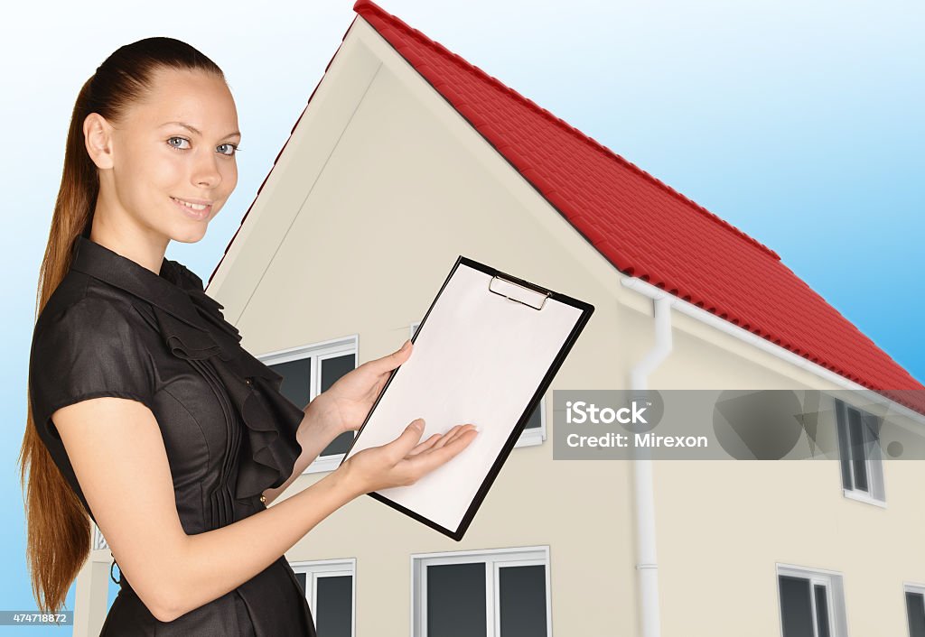 Office woman shows hand in clipboard standing on background of Office woman shows hand in clipboard standing on background of the house. 2015 Stock Photo