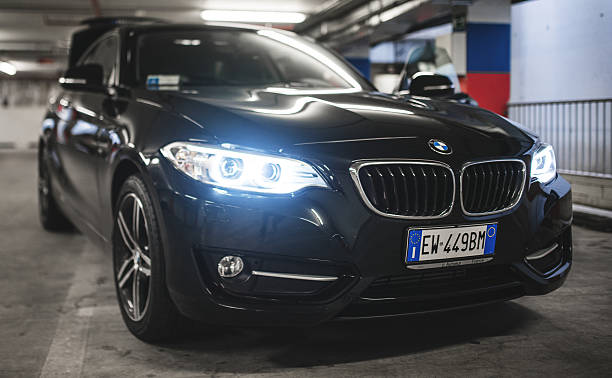 Florence, Italy - July 28, 2014: View of the new BMW 2 series (shiny black color ) parked inside a garage on Florence. This vehicle has been released to the public on late February 2014. It's the new coupe of the BMW. The focus is on the blue bi-xeno headlights.