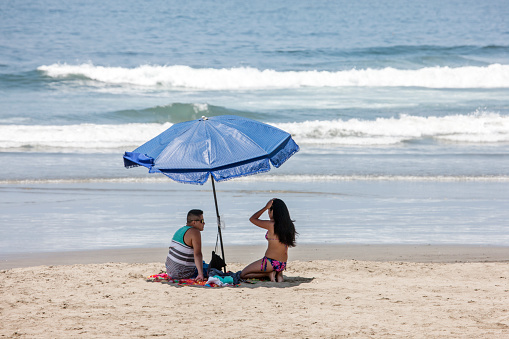 Barranca, Peru - January 22, 2015: Hispanic young adult  couple on Barranca beach underneath parasol on the Peruvian coast