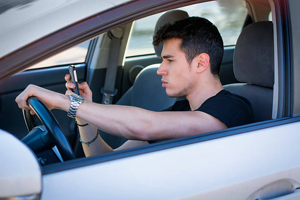 Handsome Young Man Using his Cell Phone Driving a Car Inattentive Handsome Young Man Busy with his Mobile Phone While Driving a Car. Distracted stock pictures, royalty-free photos & images