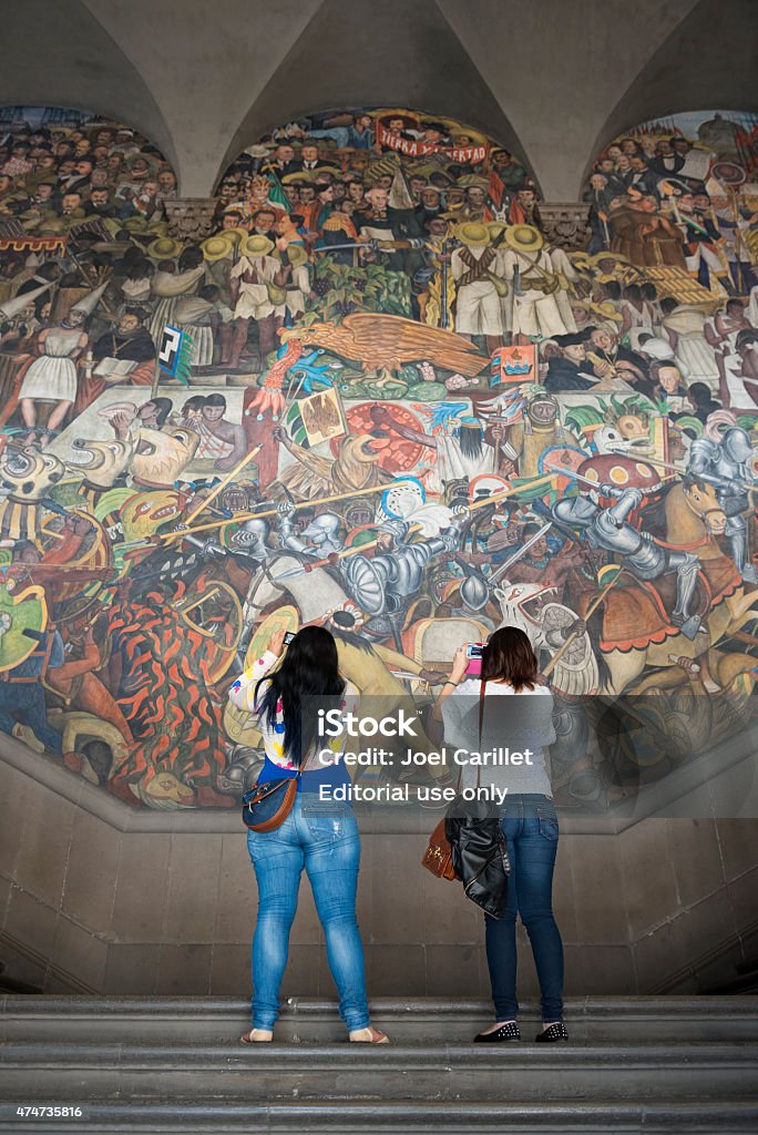 Photographing a Diego Rivera mural in Mexico City Mexico City, Mexico - October 28, 2014: Two women stand on steps at the National Palace in Mexico City, Mexico, using their smartphones to photograph a mural by Diego Rivera, one of several painted between 1929 and 1951. The open-air murals are one of the most visited attractions in Mexico City; entrance is free. Diego Rivera Stock Photo