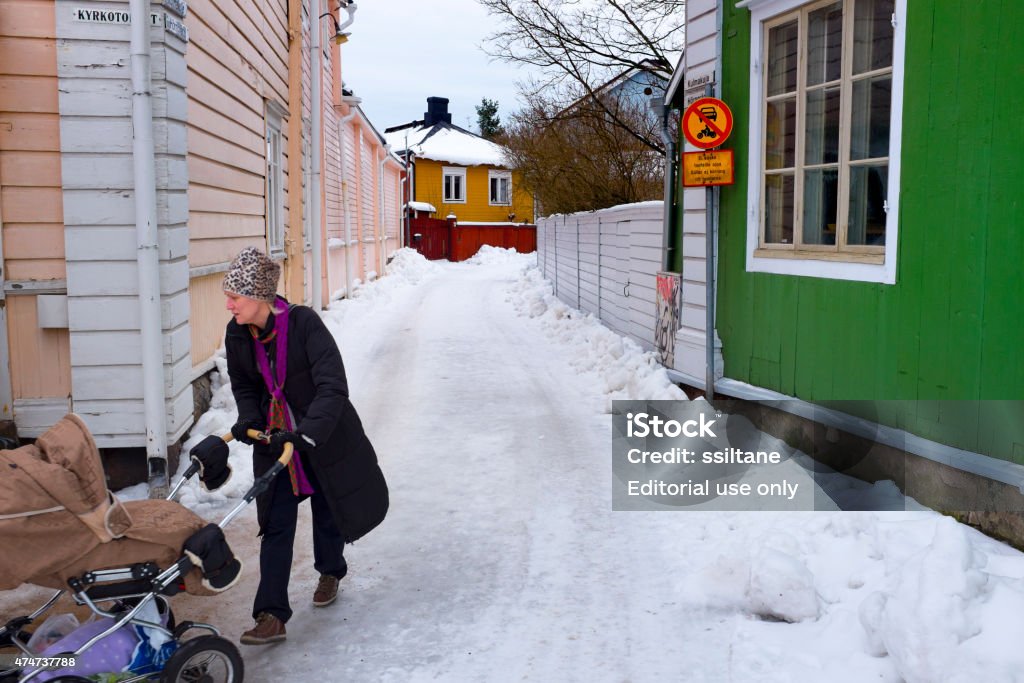 Woman and stroller in wooden Porvoo, Finland Porvoo, Finland - February 7, 2015: woman with a stroller walking along a snowy alley in the colourful wooden Old City of Porvoo. The picture was taken on the Church Square of Porvoo. 2015 Stock Photo