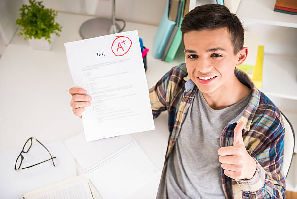 Schoolboy Portrait of teenager sitting at the table at home and showing perfect test results. homework paper stock pictures, royalty-free photos & images