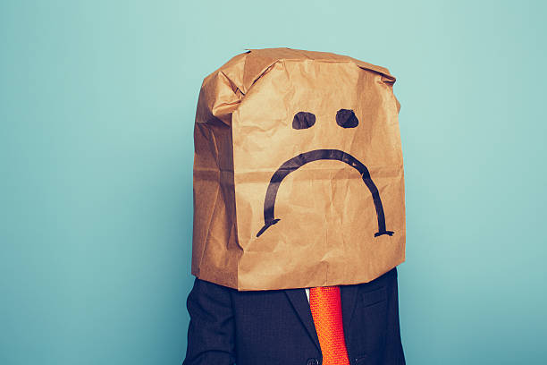 Young Boy Businessman Wears Sad Face A young boy dressed as a businessman wears a paper bag with a sad face on it The economy has pushed his business down. He sits at his desk with retro computer and phone. conscious stock pictures, royalty-free photos & images
