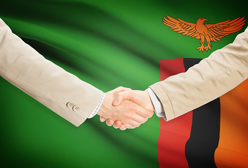 Businessmen shaking hands with flag on background - Zambia