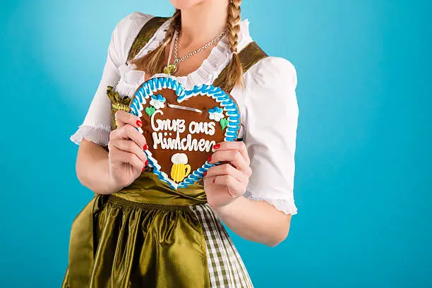 Young woman in traditional Bavarian clothes - dirndl or tracht with a gingerbread souvenir heart