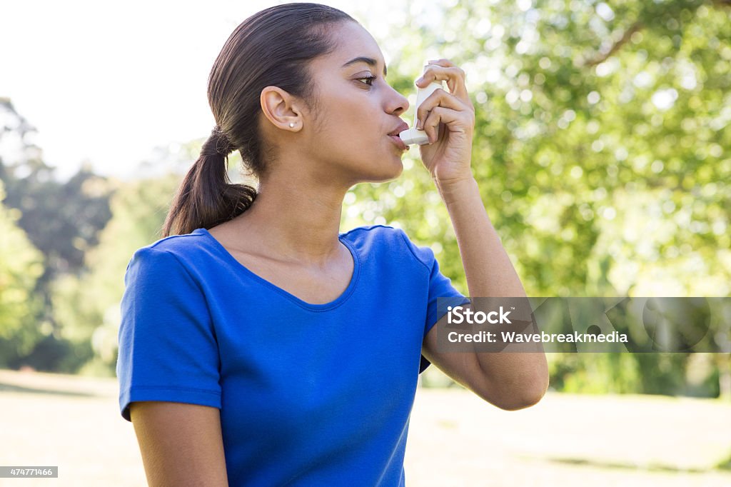 Pretty woman using her inhaler Pretty woman using her inhaler on a sunny day Asthmatic Stock Photo