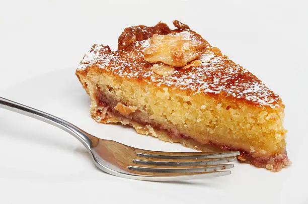 Closeup of a slice of Bakewell tart on a plate with a fork in the foreground
