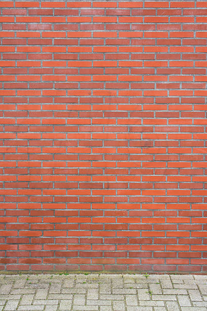 istock Red brick wall on grey street stones with some weeds 474784502