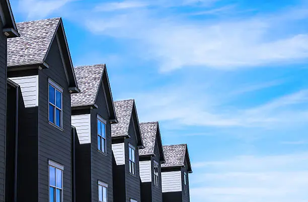 greenish blue row homes in a line against a bright blue sky with clouds and shadows