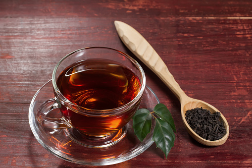 Cup of hot black tea with leaf on wooden table