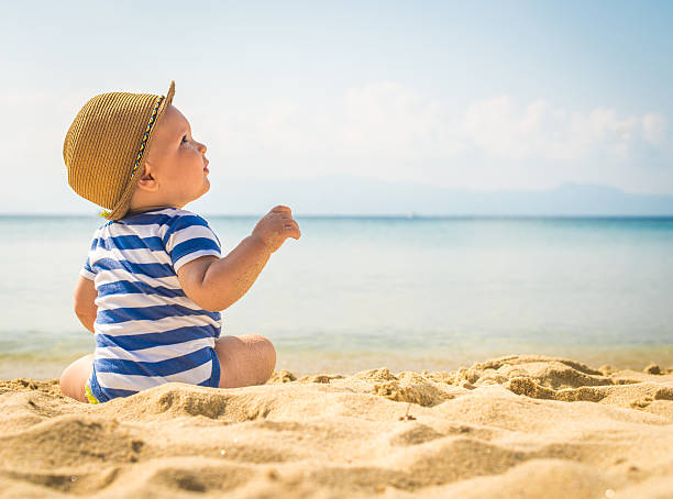 Little baby boy sitting on the sand The cute baby boy playing on the beach. Little boy sitting on the sand. Sea and seashore as background with copy space children at the beach stock pictures, royalty-free photos & images