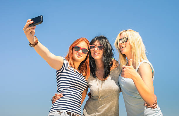 fidanzate felice prendendo selfie contro il cielo blu - women smiling body cheerful foto e immagini stock