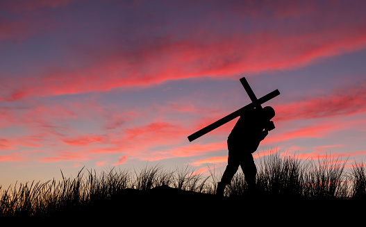 Man with a carrying a cross on his back at sunrise.