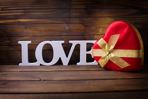Word love and gift box in form of heart  on wooden background. Selective focis is on word love.