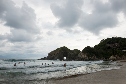 Zipolite, Mexico - November 9, 2014: People, including nude swimmers, enjoy the beach despite the dark rain clouds filling the sky in Zipolite, on the Pacific coast of Oaxaca State, Mexico.