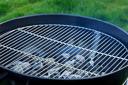 Full shot of a BBQ pit filled with lit charcoals. The BBQ is standing in a garden outside a residential property. The house is located in Newcastle Upon Tyne.\n\nVideos are available similar to this scenario