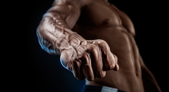 Handsome muscular bodybuilder demonstrates his fist and vein, blood vessels. Studio shot on black background.