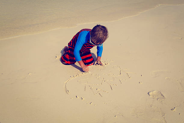 istock little boy drawing family on the beach 474849622
