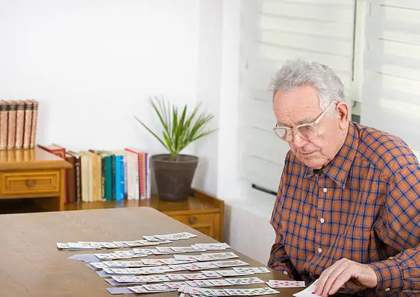 Old man playing solitaire with cards at dining table